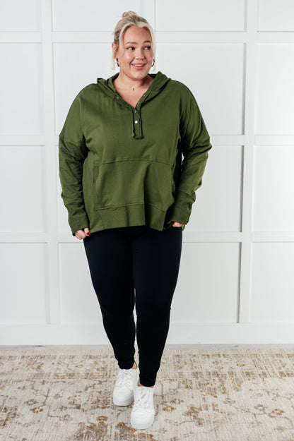 Person wearing a green hoodie and black pants against a white paneled wall.