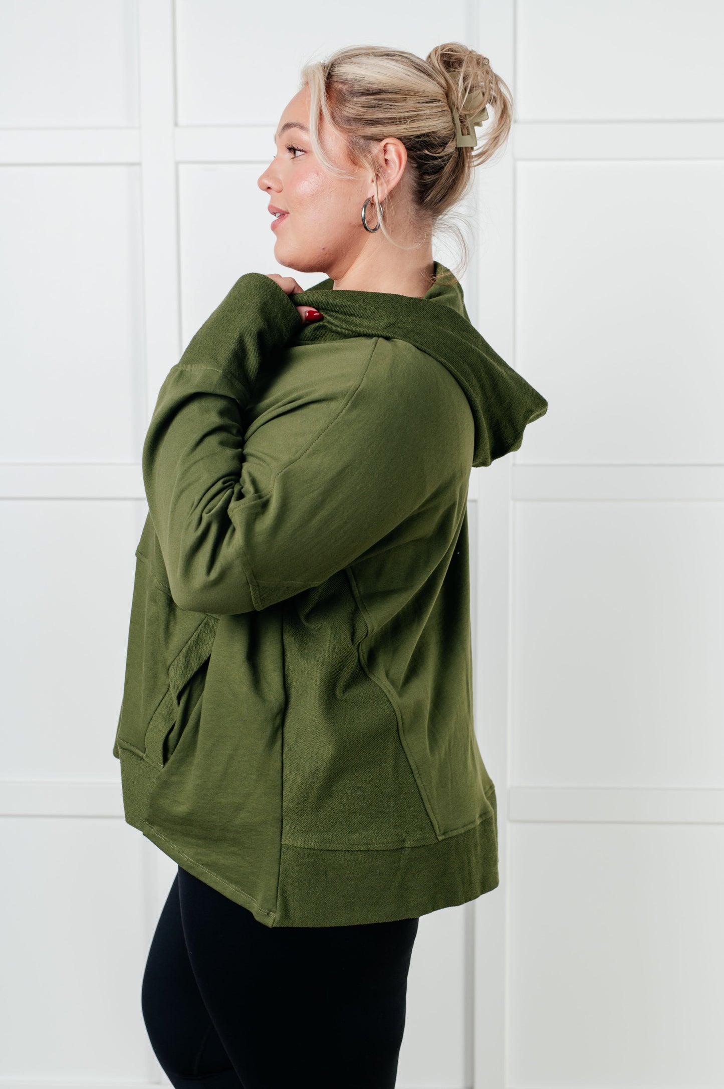 Woman wearing an olive green jacket against a white tiled wall