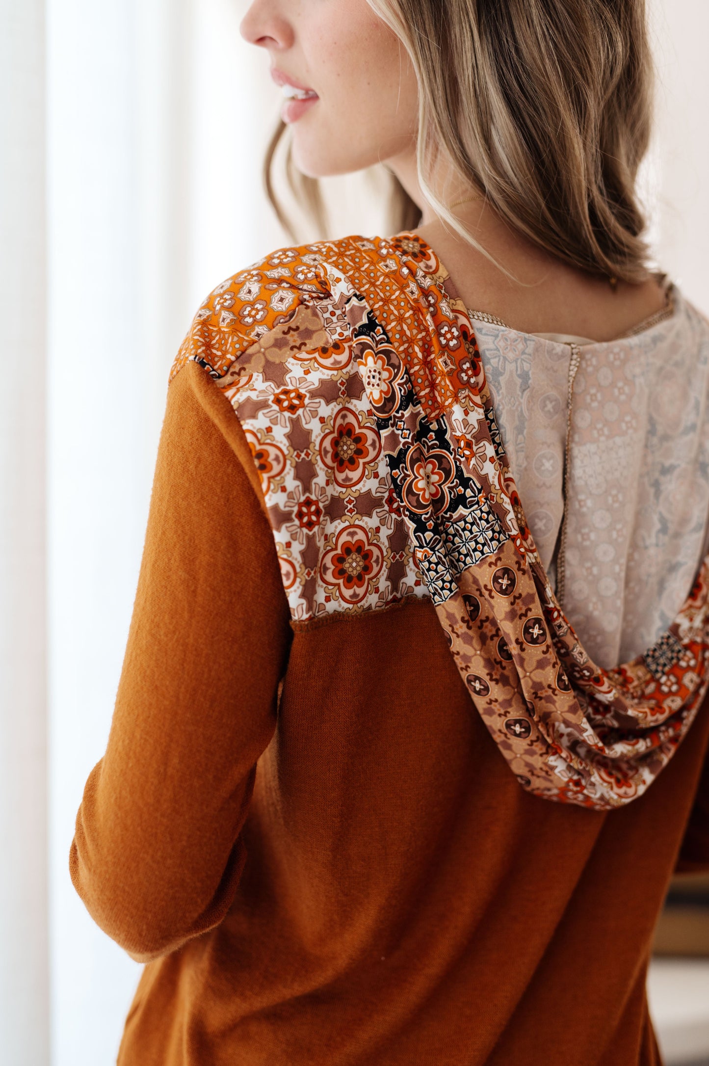 Close-up of a person wearing a brown top with floral embroidery and a beige patterned garment underneath.