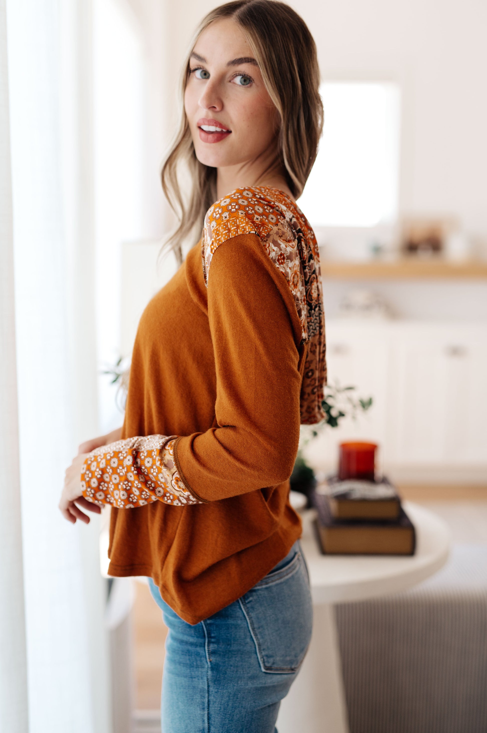 Woman wearing a mustard yellow sweater with patterned sleeves in a bright room.