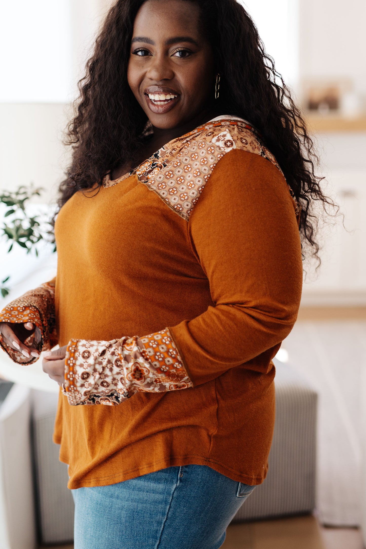Woman wearing a mustard yellow top with patterned cuffs in a bright room.