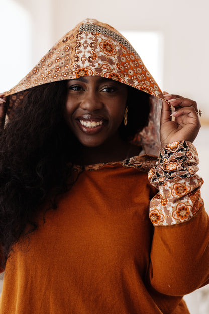 Woman wearing a brown outfit with a decorative hood against a neutral background