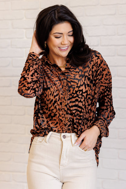 Woman wearing a leopard print blouse and beige pants against a white brick wall.