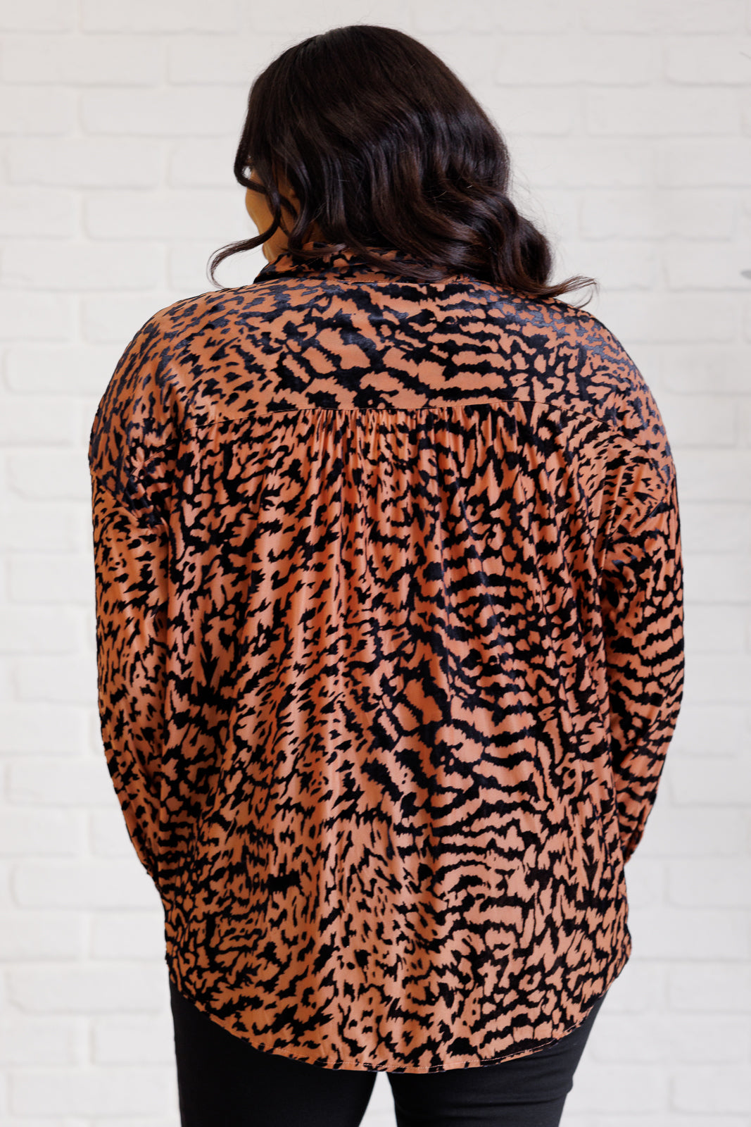 Person wearing a leopard print top against a white brick wall.