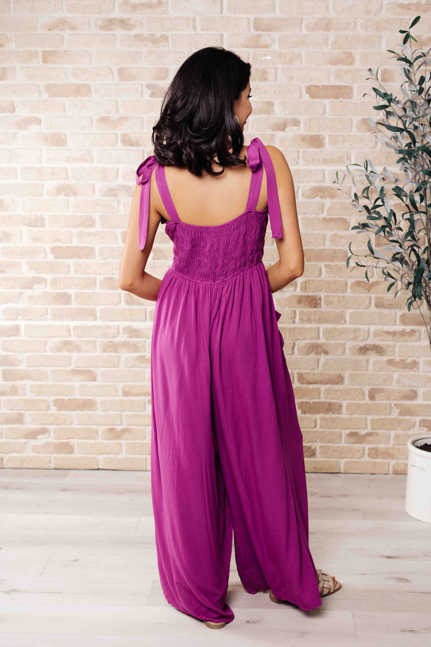 Woman wearing a purple jumpsuit with a brick wall background