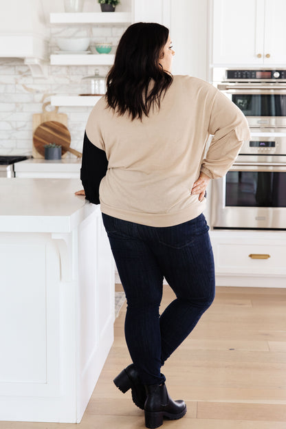 Person standing in a kitchen wearing a beige sweater and dark jeans.