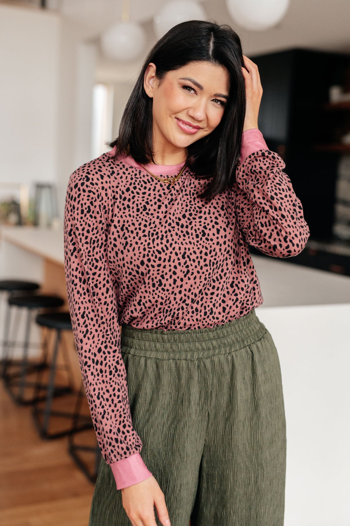Woman wearing a pink leopard print sweater and green pants in a kitchen setting