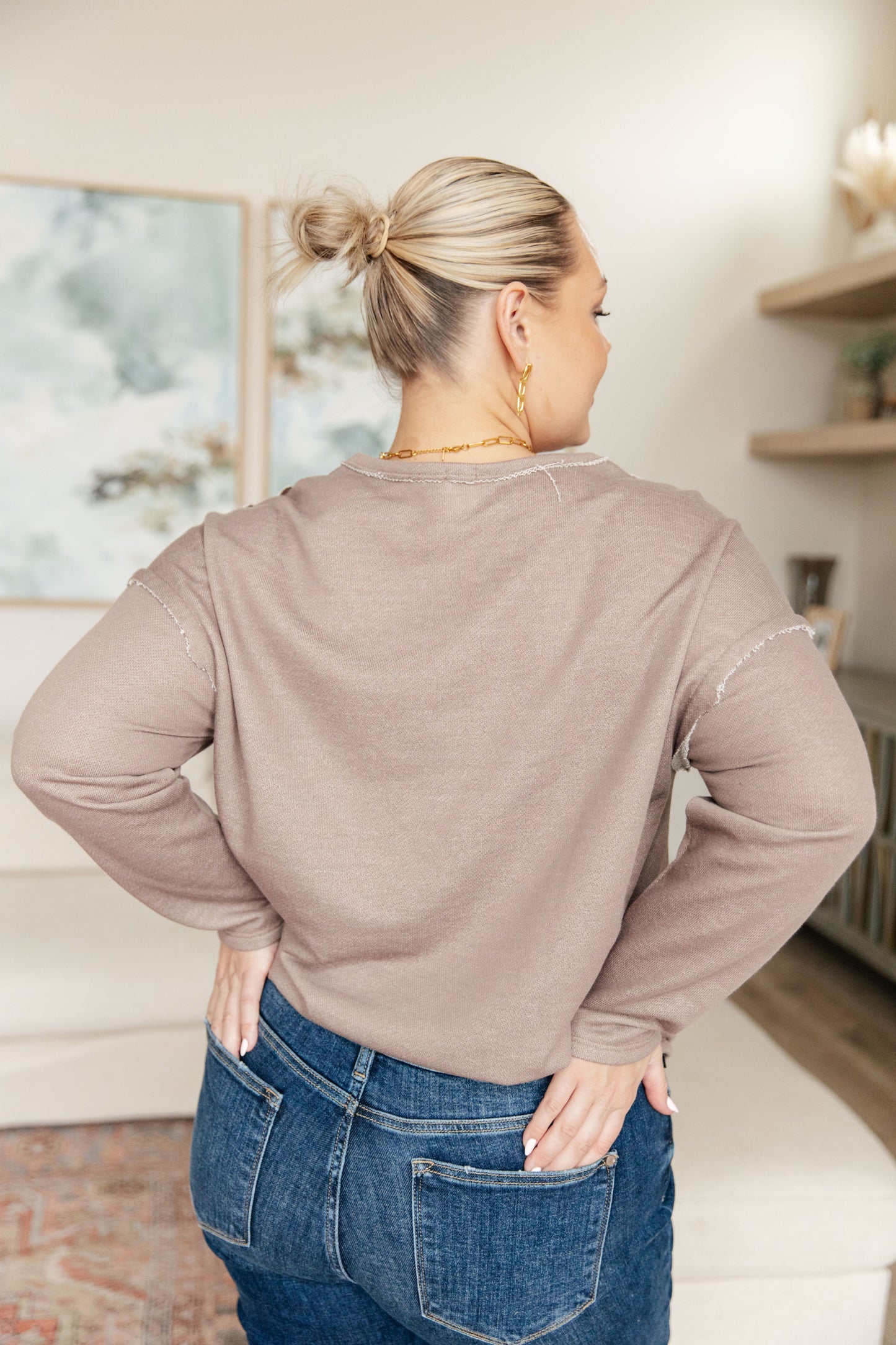 Woman wearing a beige sweater and blue jeans in an indoor setting