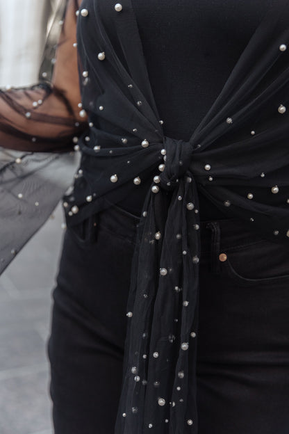 Black top with pearl embellishments on a blurred background