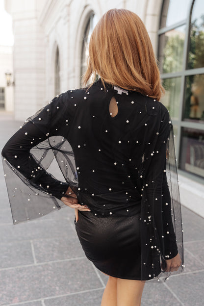 Woman wearing a black outfit with sheer sleeves and a leather skirt in an urban setting.