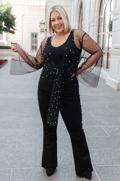 Woman wearing a black outfit with sheer sleeves and sequin details outdoors.