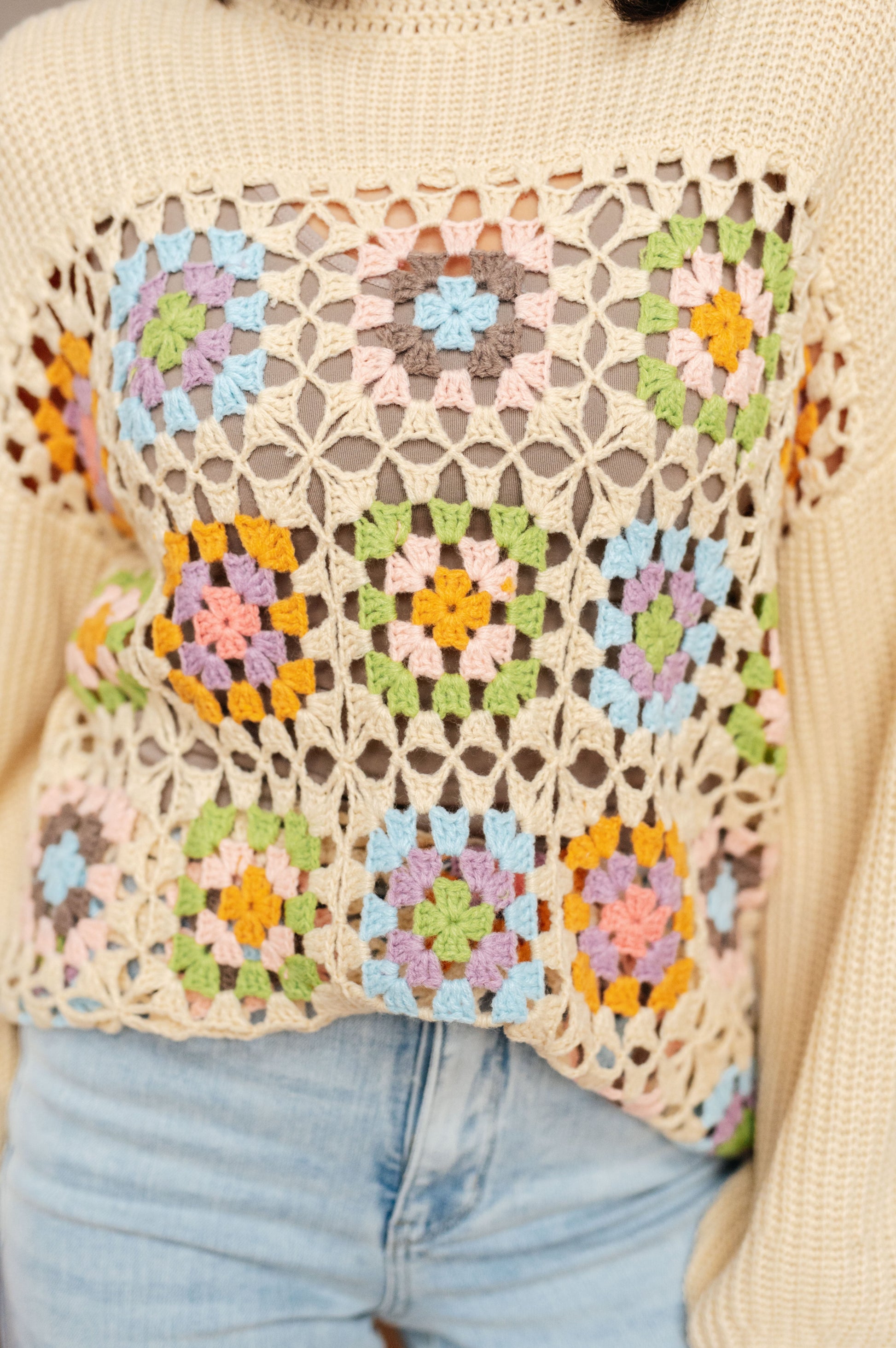 Colorful crochet patterned bag held by a person wearing a beige sweater.