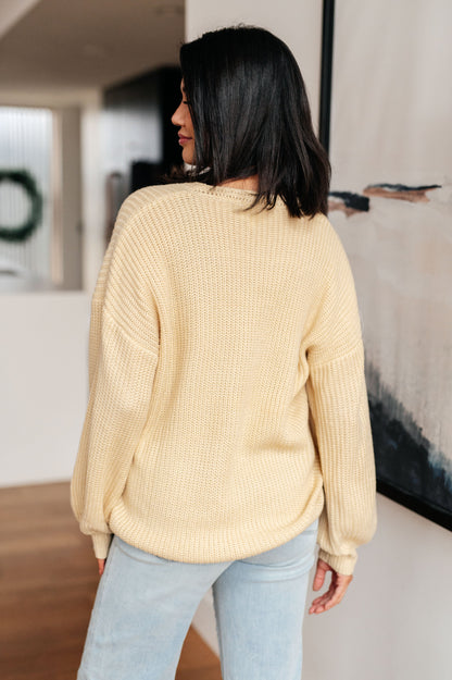 Woman wearing a beige sweater and light blue jeans in an indoor setting.