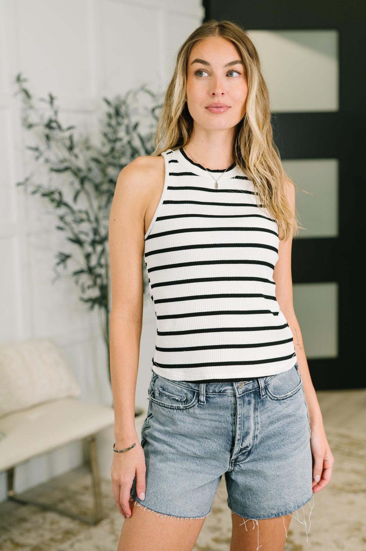 Woman wearing a striped tank top and denim shorts indoors.