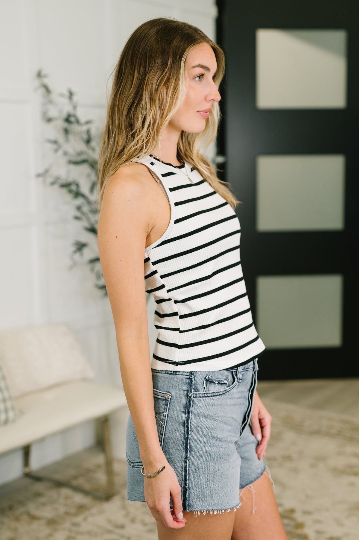 Woman wearing a black and white striped tank top and denim shorts in an indoor setting.