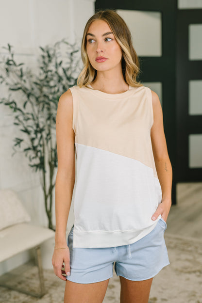 Woman wearing a beige and light gray sleeveless top with light blue shorts indoors.