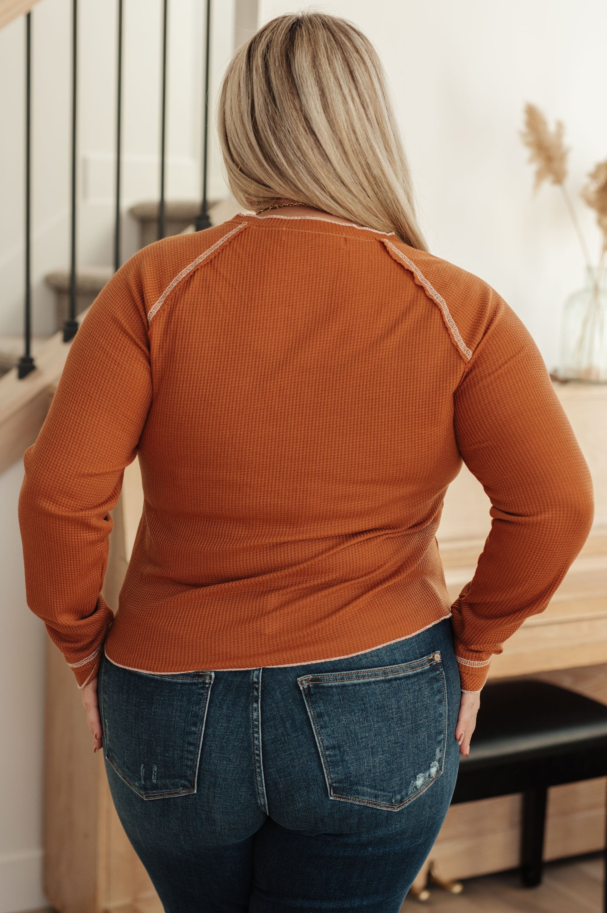 Person wearing a rust-colored long-sleeve top and blue jeans in an indoor setting.