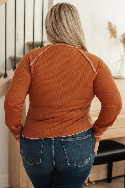 Person wearing a rust-colored long-sleeve top and blue jeans in an indoor setting.