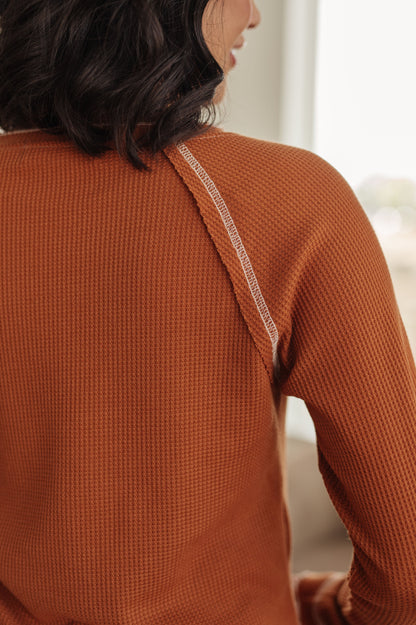 Person wearing a rust-colored textured sweater with thin straps.