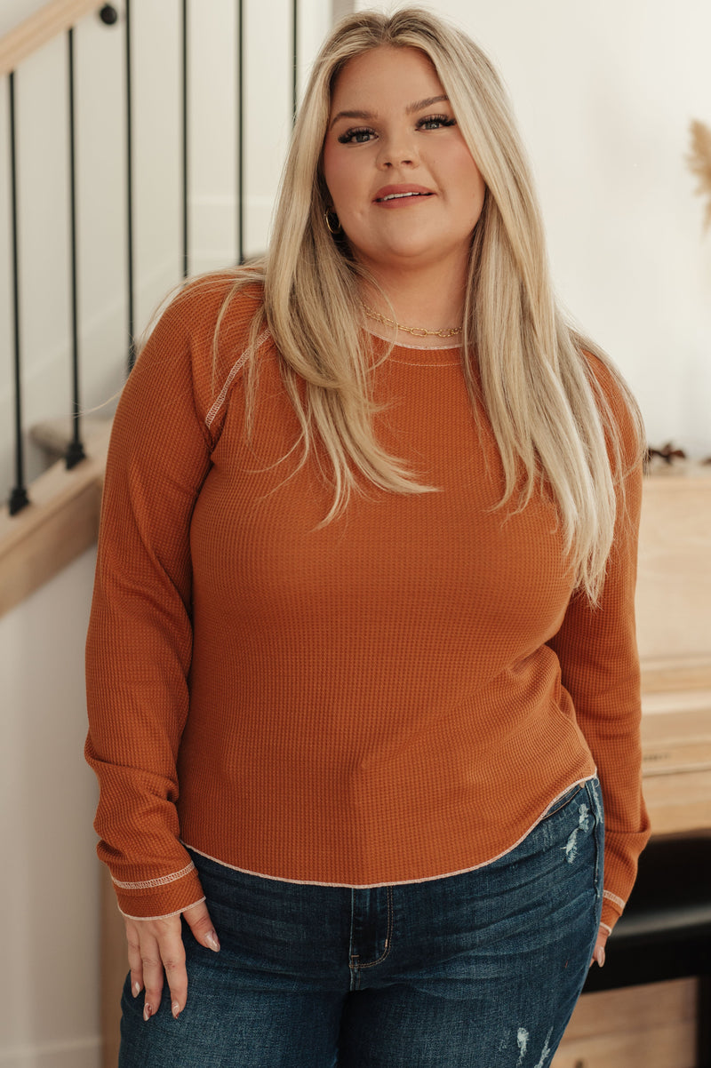 Woman wearing an orange sweater and blue jeans indoors.
