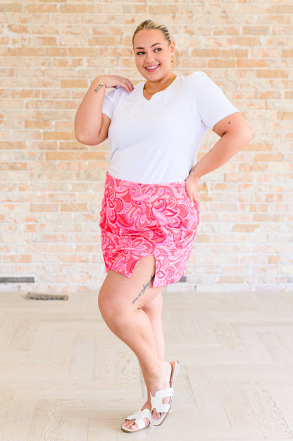 A woman wearing a white v-neck tee shirt and a pink paisley mini skirt.