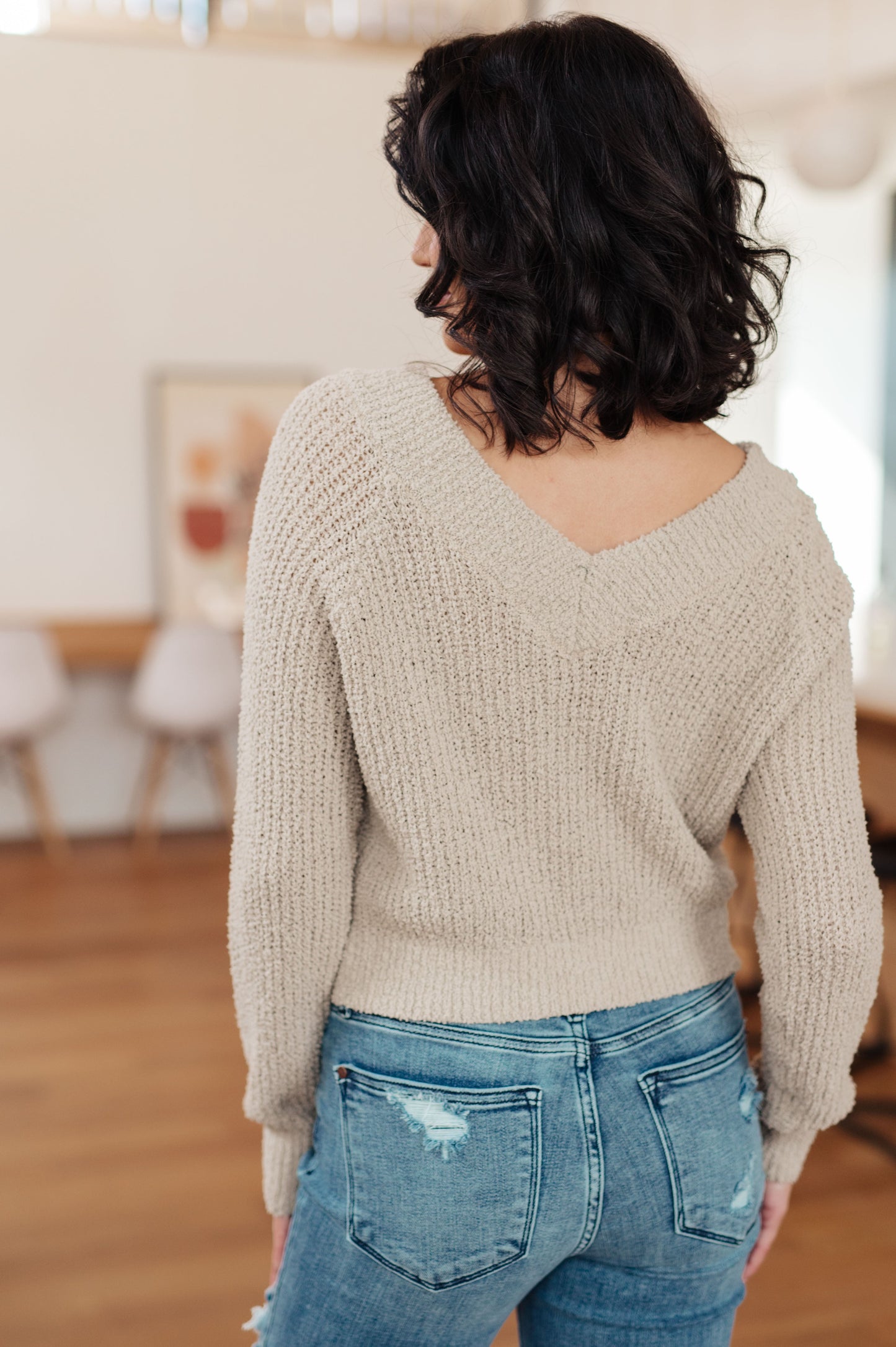 Person wearing a beige sweater and blue jeans in an indoor setting