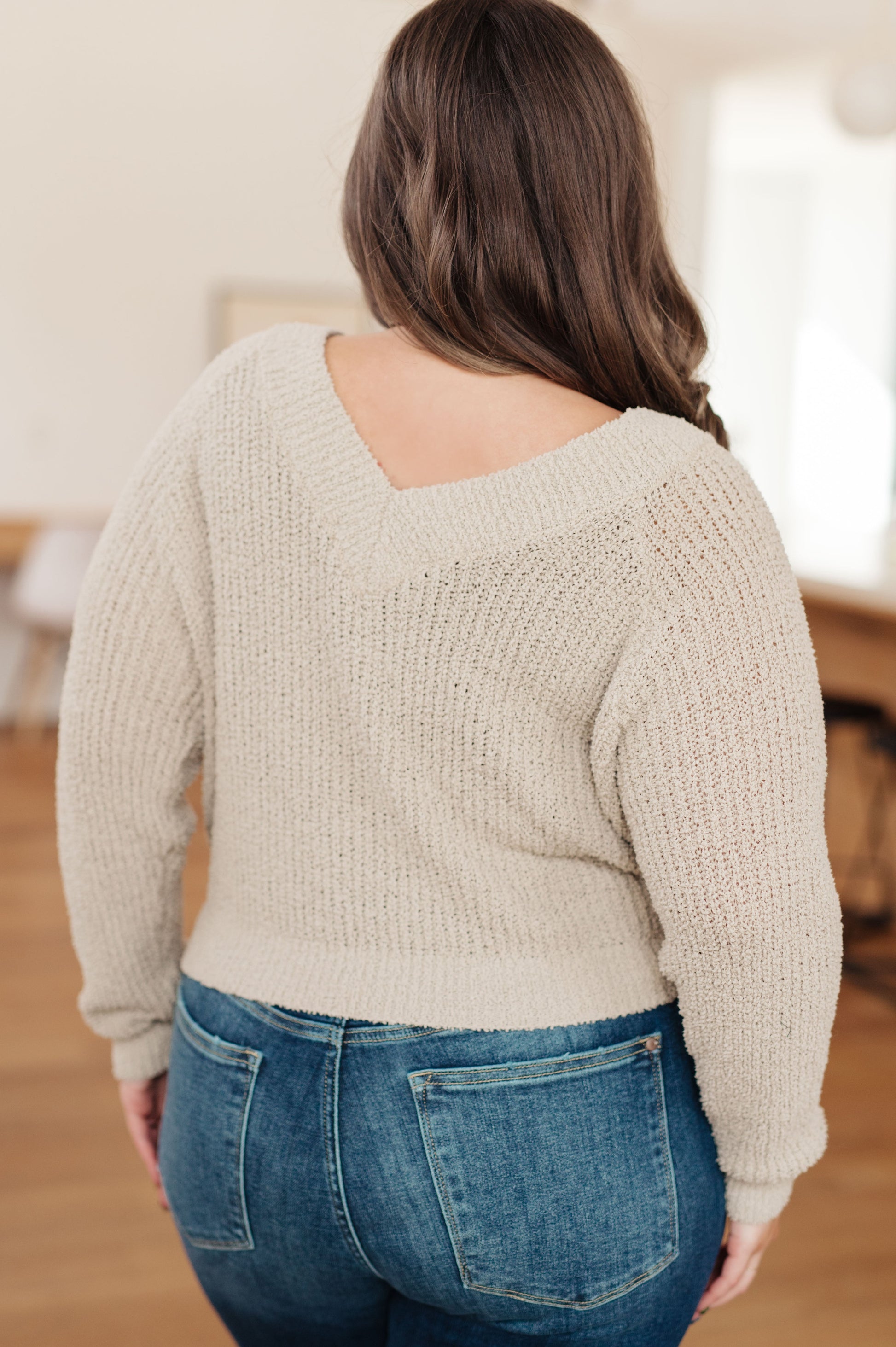 Person wearing a beige sweater and blue jeans from behind