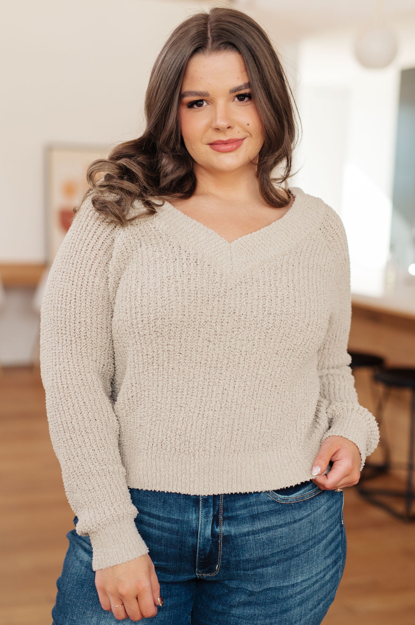 Woman wearing a beige sweater and blue jeans indoors