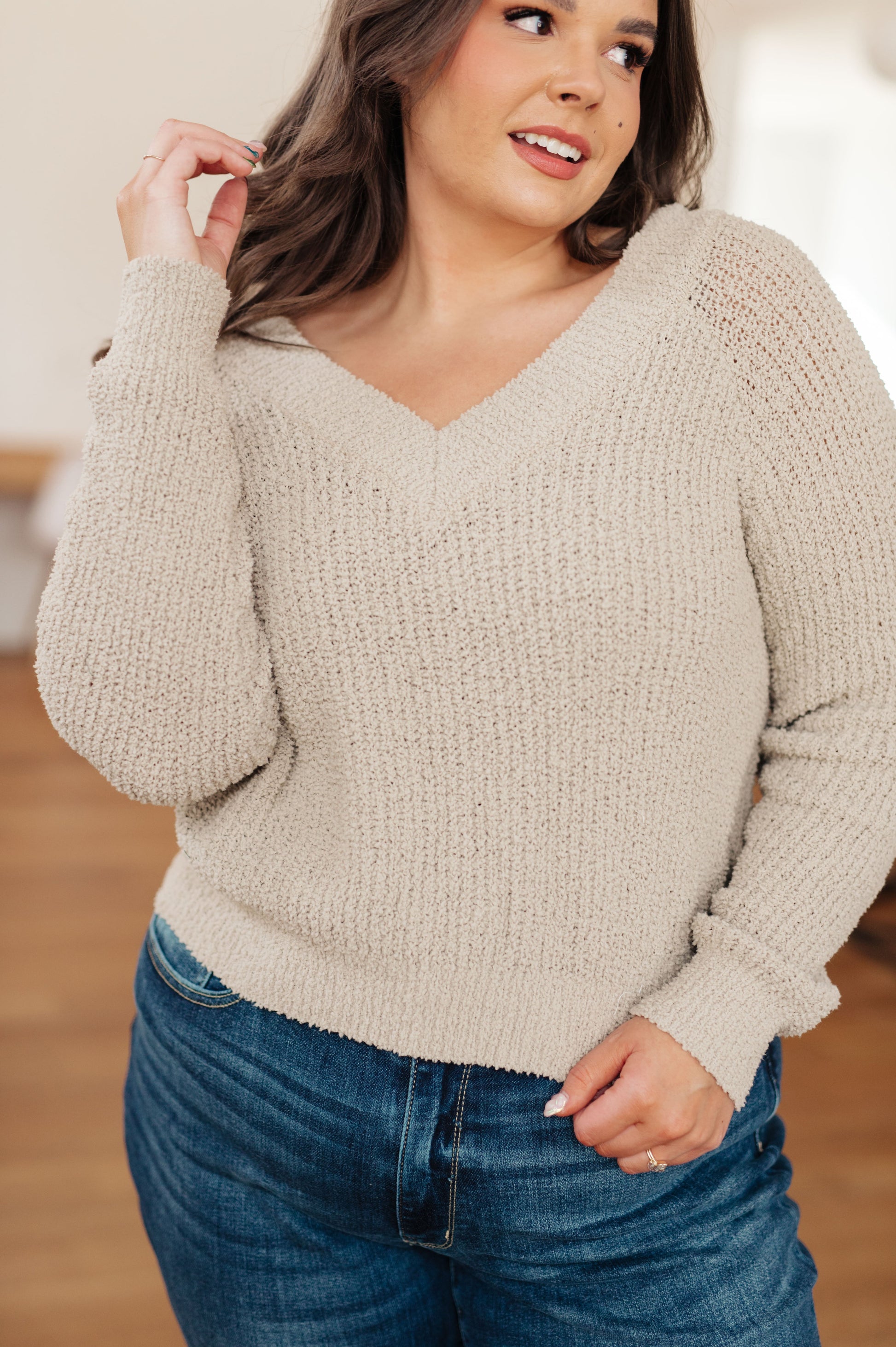 Woman wearing a beige sweater and blue jeans indoors
