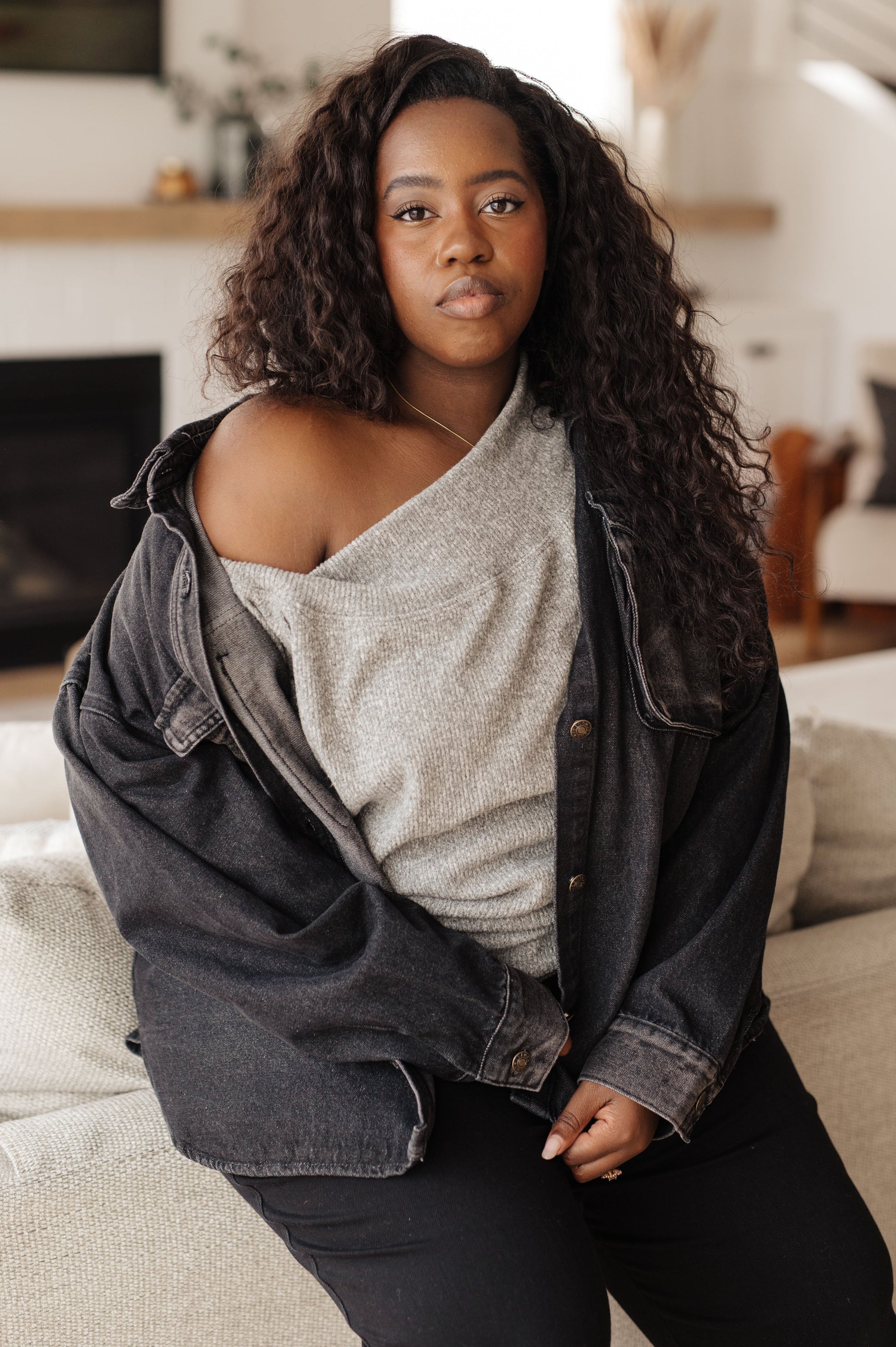 Woman wearing a gray sweater and black jacket in a living room setting
