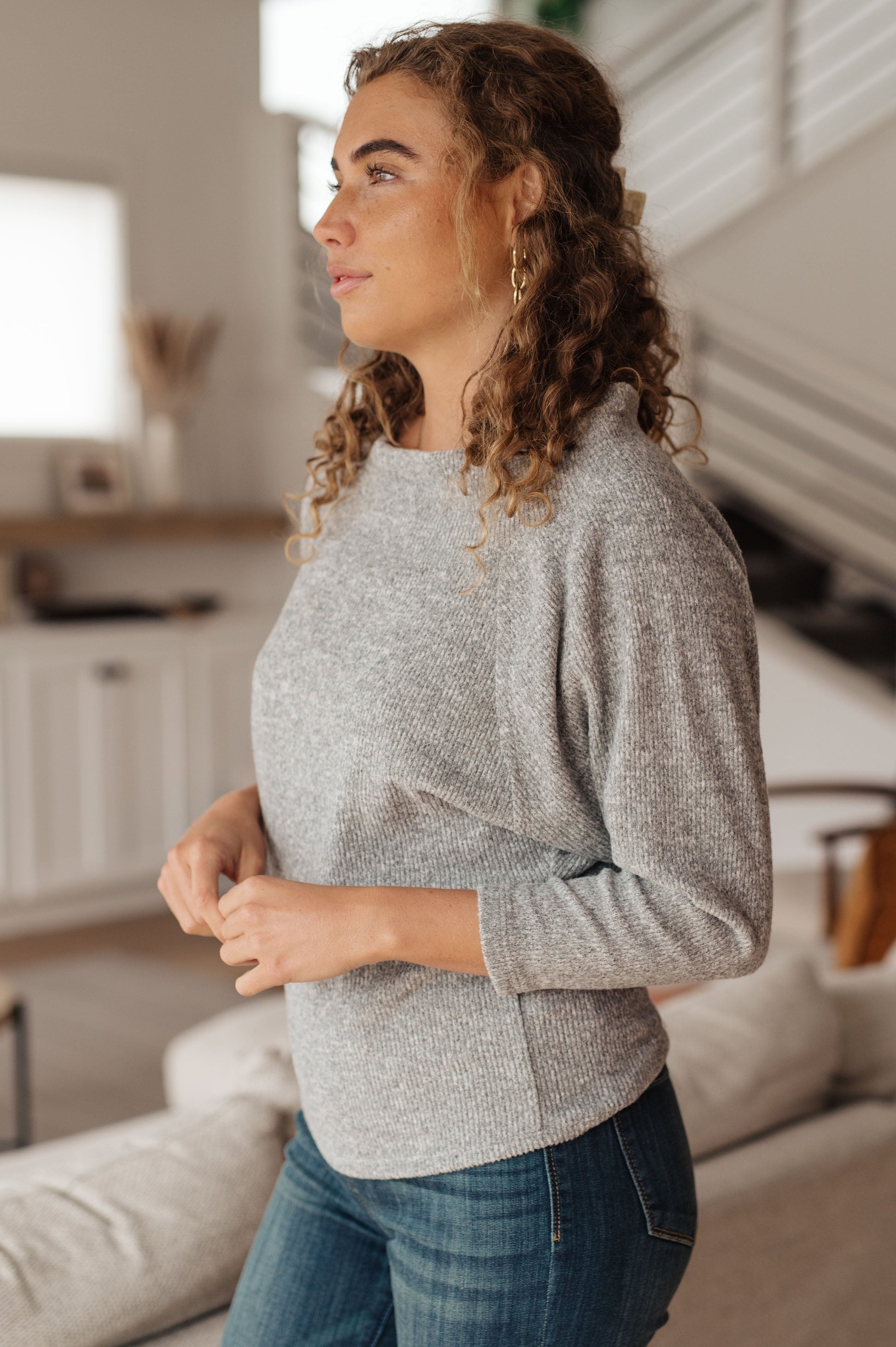 Woman wearing a gray sweater and blue jeans standing in a living room.
