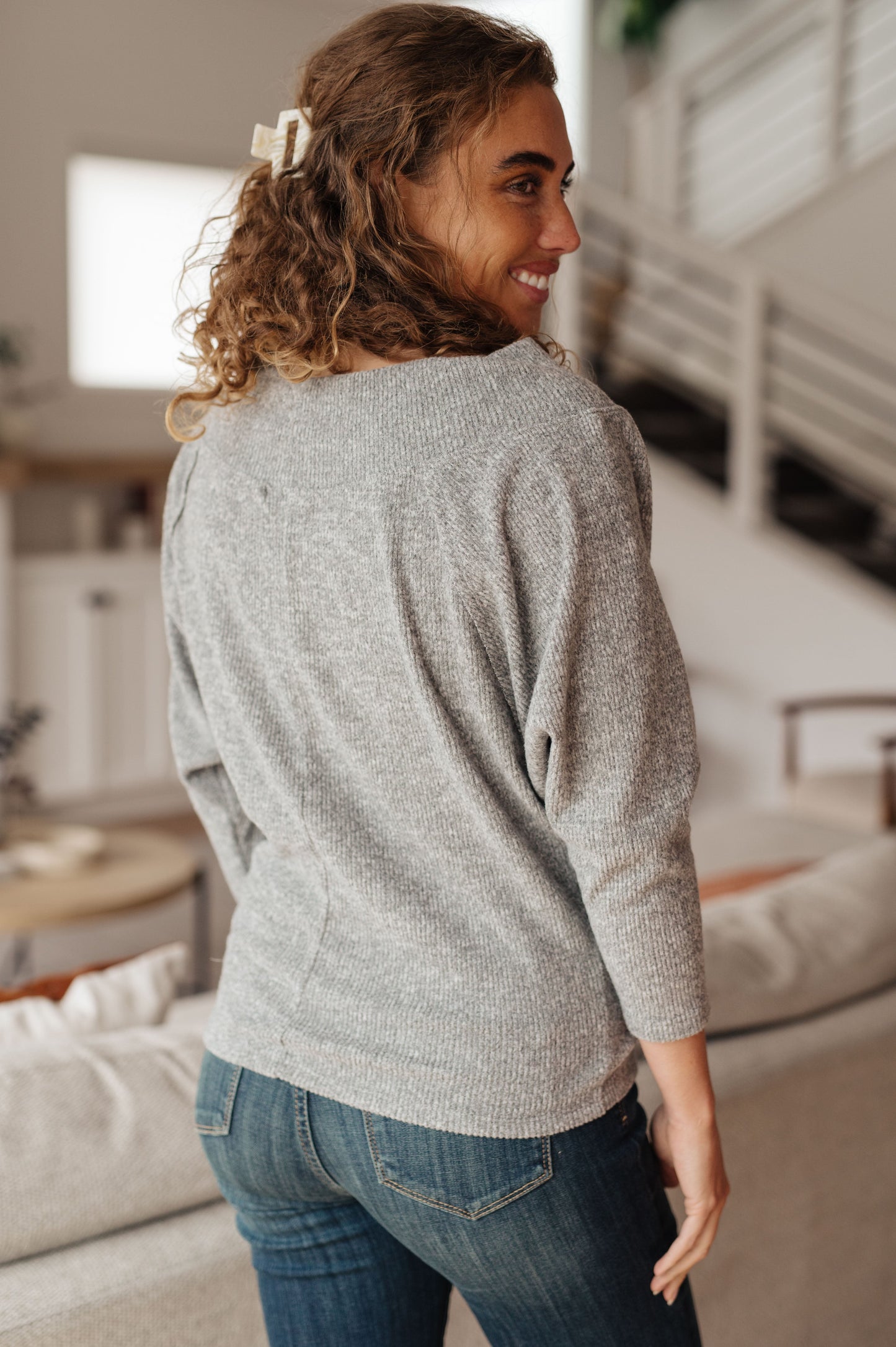 Woman wearing a gray sweater and blue jeans in a living room.