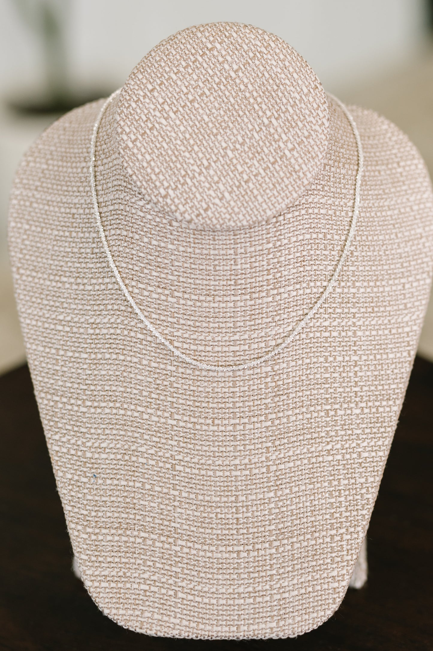 Silver beaded necklace on a mannequin bust against a blurred background