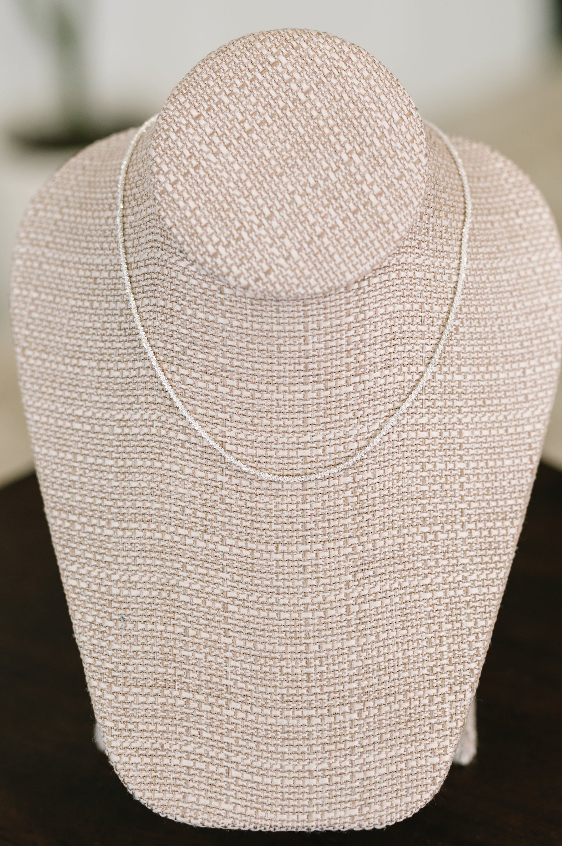 Silver beaded necklace on a mannequin bust against a blurred background