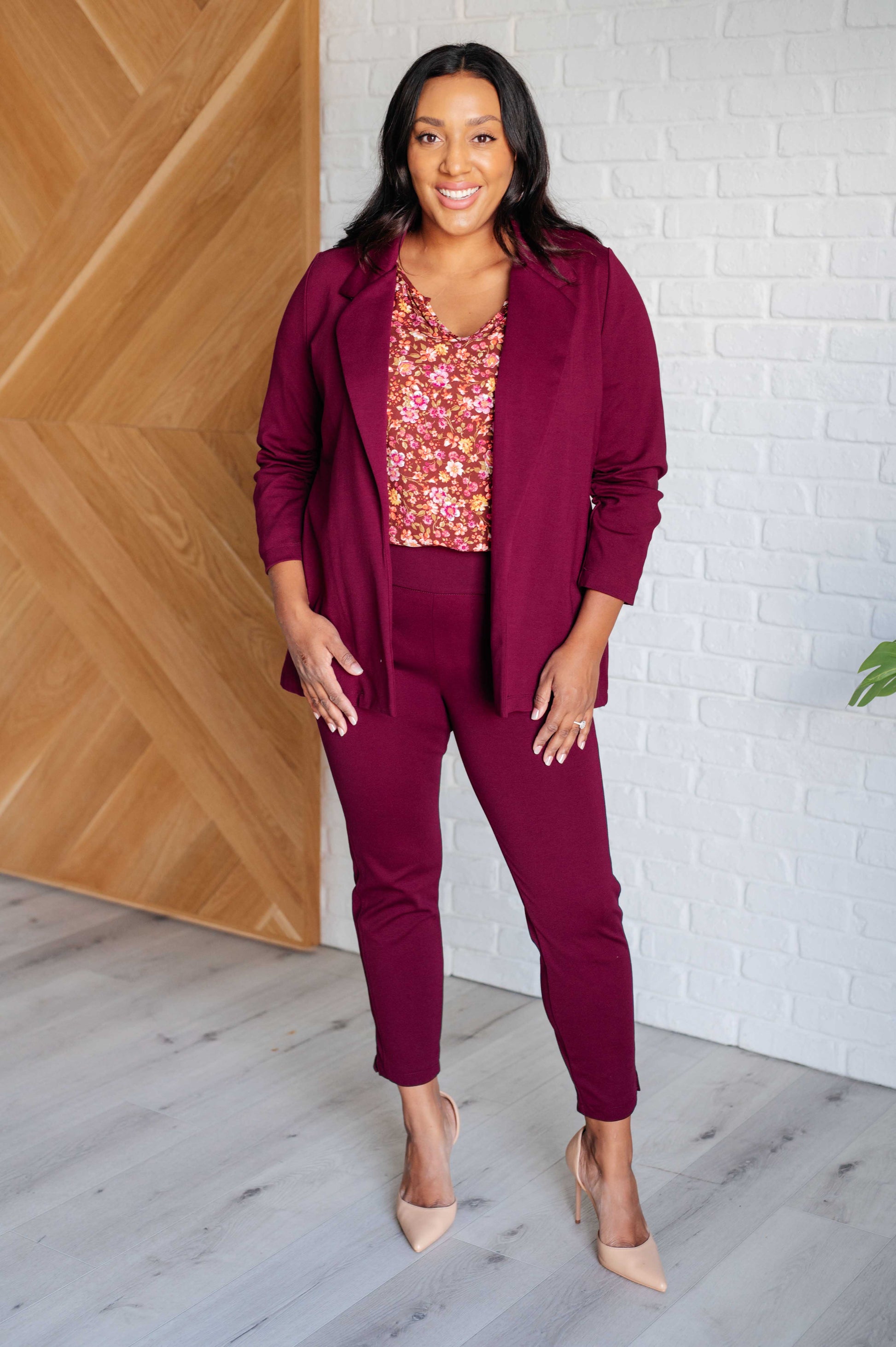 Woman in a maroon outfit standing against a white brick wall.