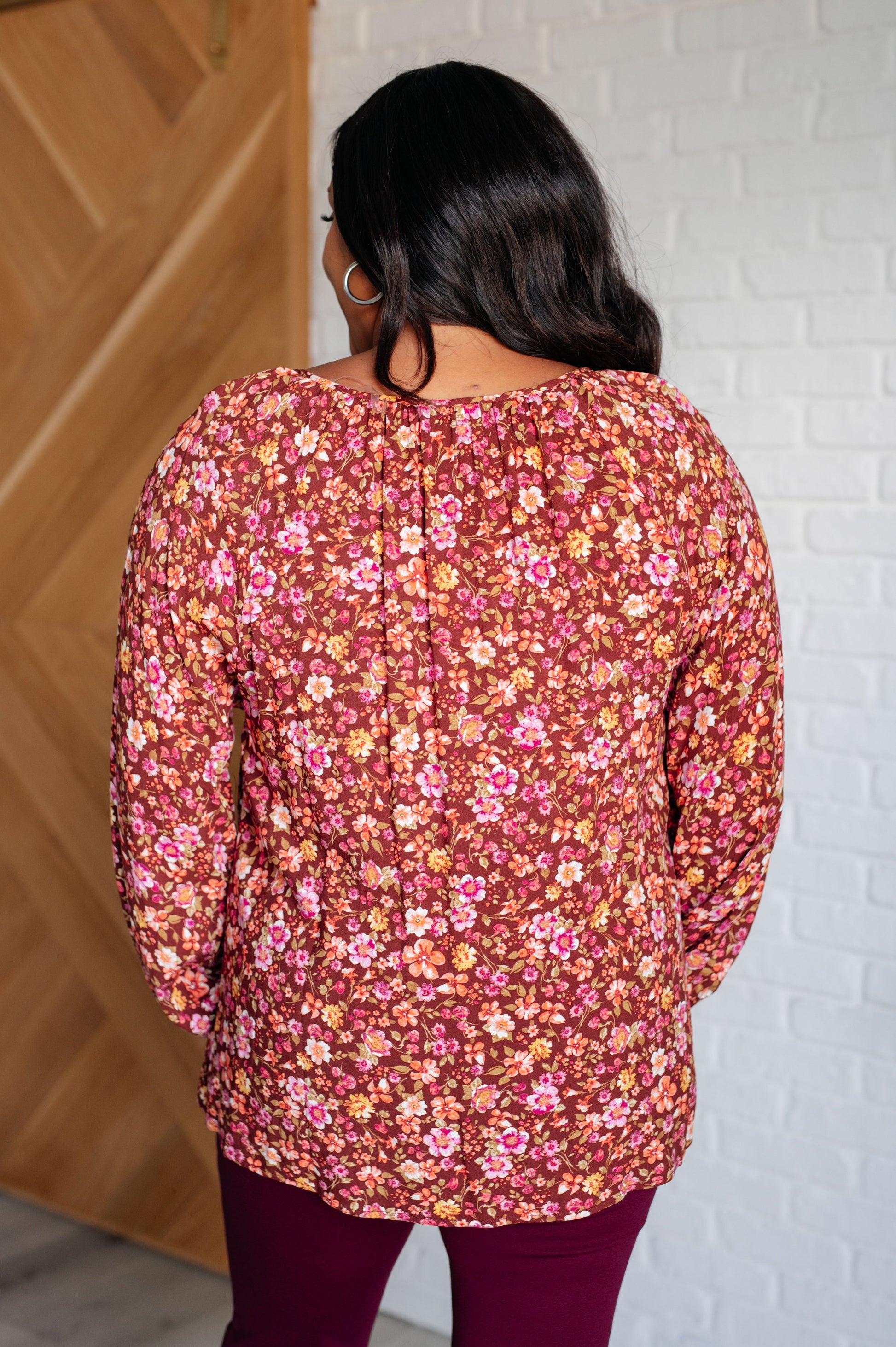 Person wearing a floral long-sleeve top against a white brick wall.