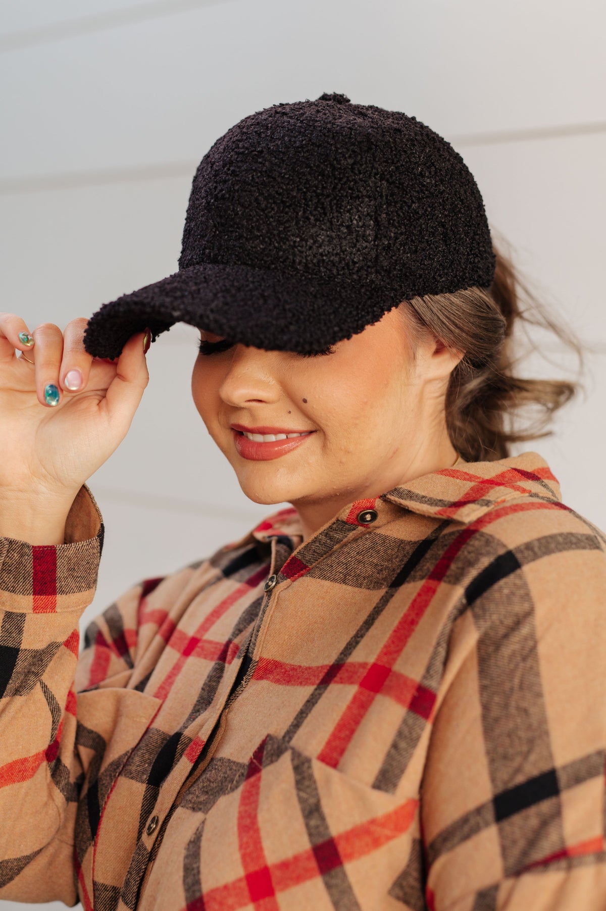 Woman wearing a black cap and plaid shirt against a neutral background
