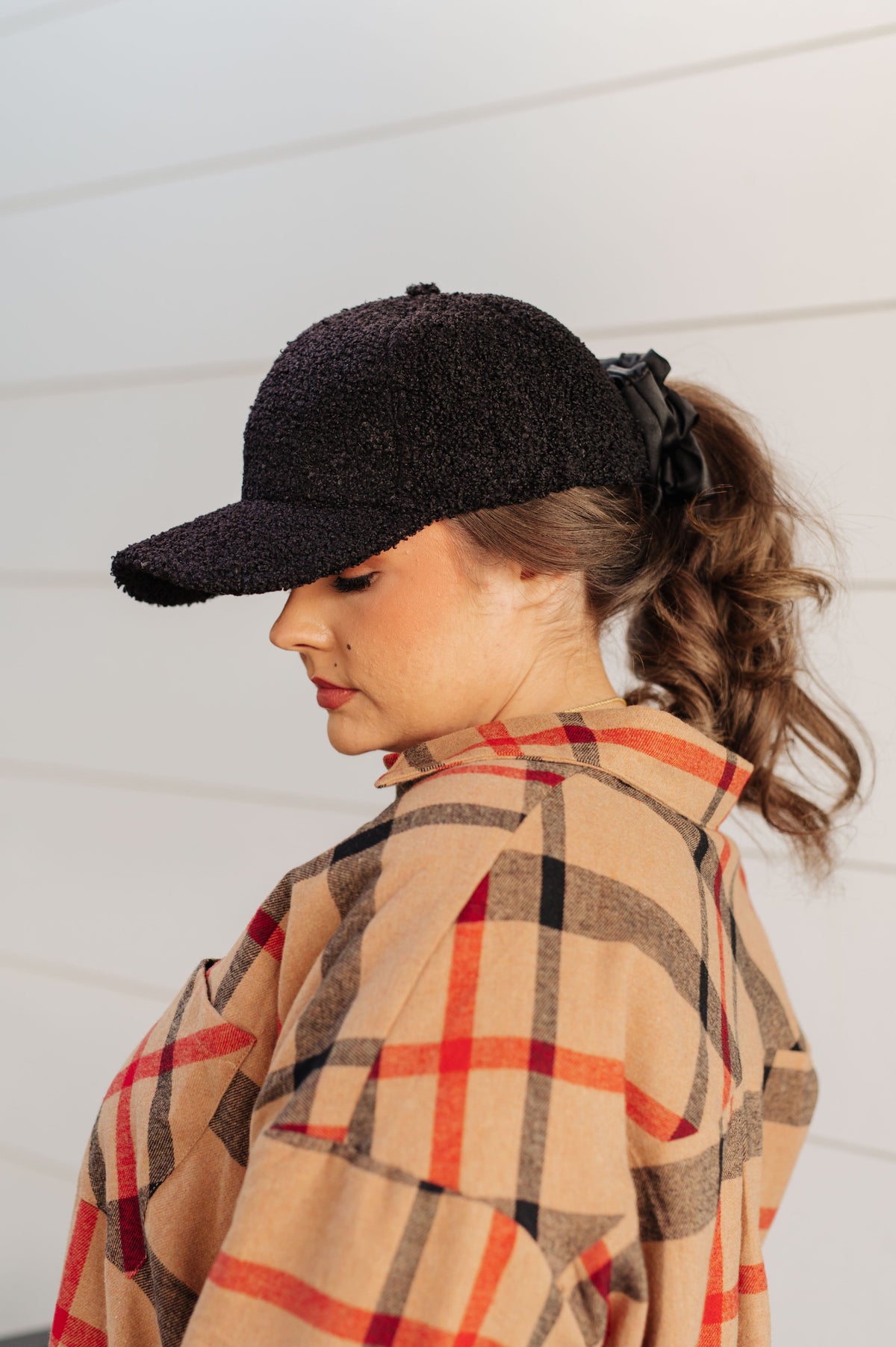 Woman wearing a black cap and plaid shirt against a white wall