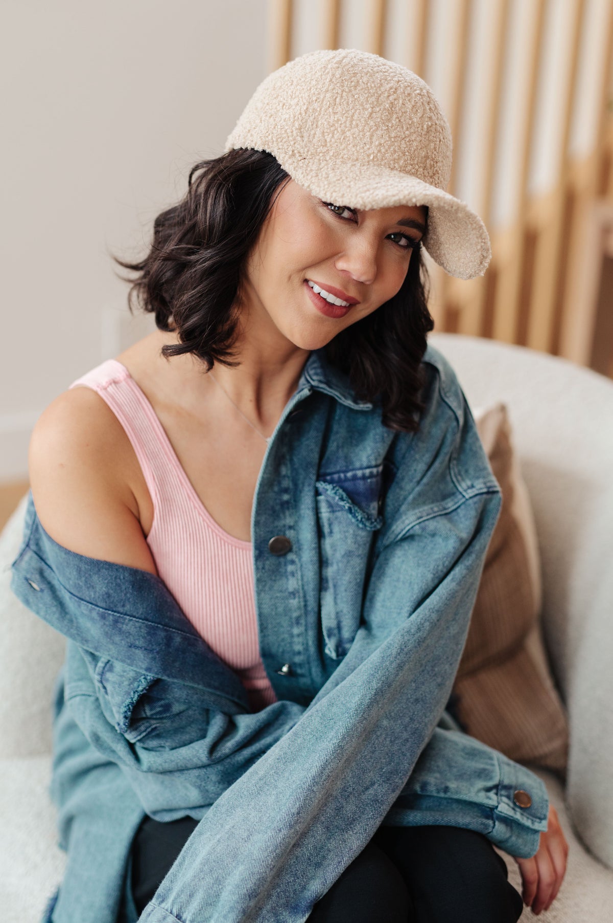 Woman wearing a beige cap and denim jacket sitting on a couch.