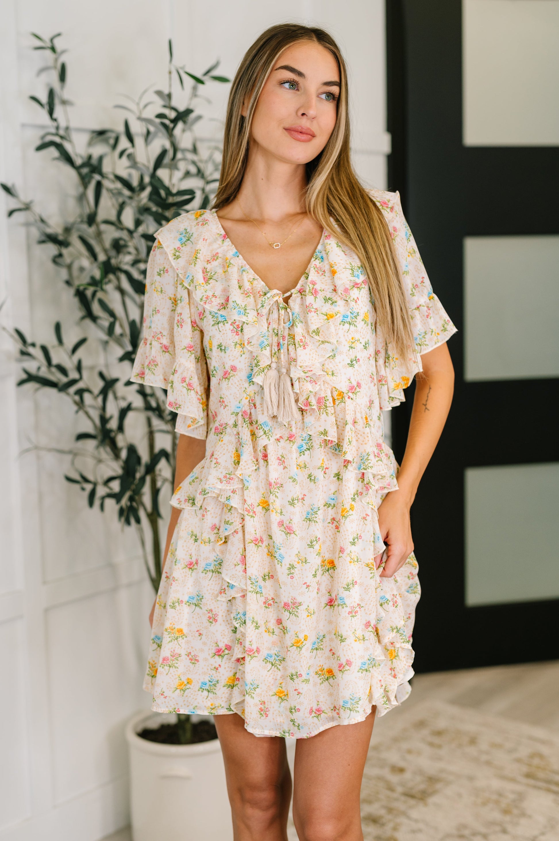 Woman wearing a floral dress standing indoors with a plant in the background