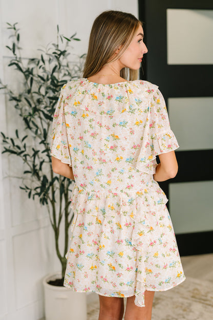 Woman wearing a floral dress standing in a room with a plant and wall art.