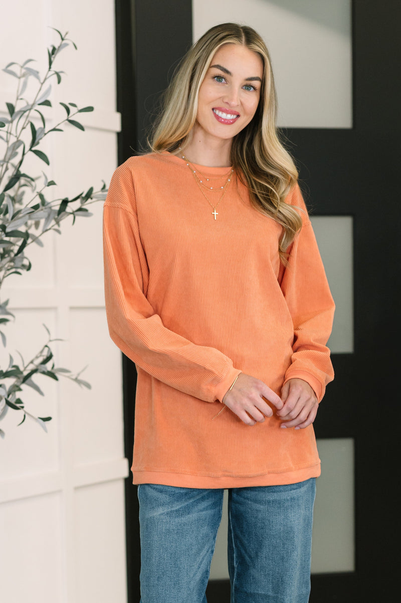 Woman wearing an orange long-sleeve top and blue jeans standing indoors.