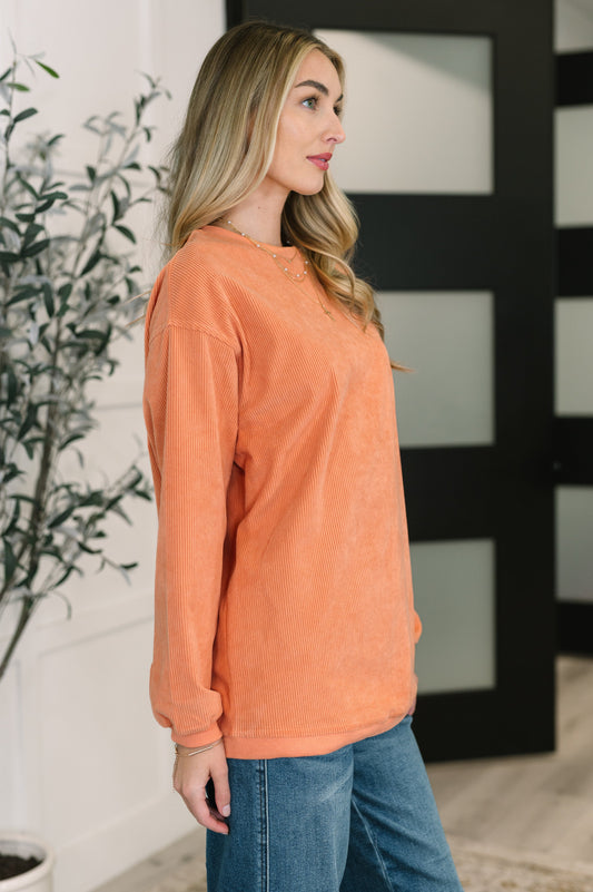 Woman wearing an orange sweatshirt and blue jeans standing indoors.