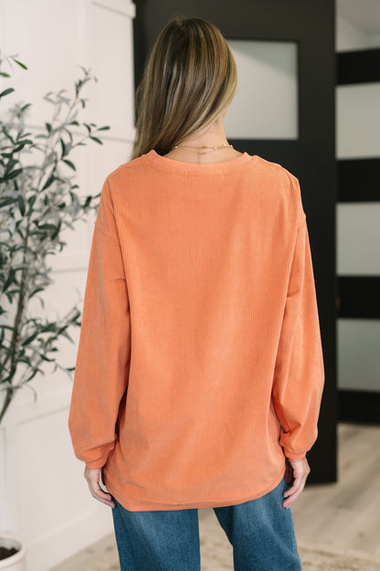 Person wearing an orange sweater and blue jeans in a room with a plant and mirror.