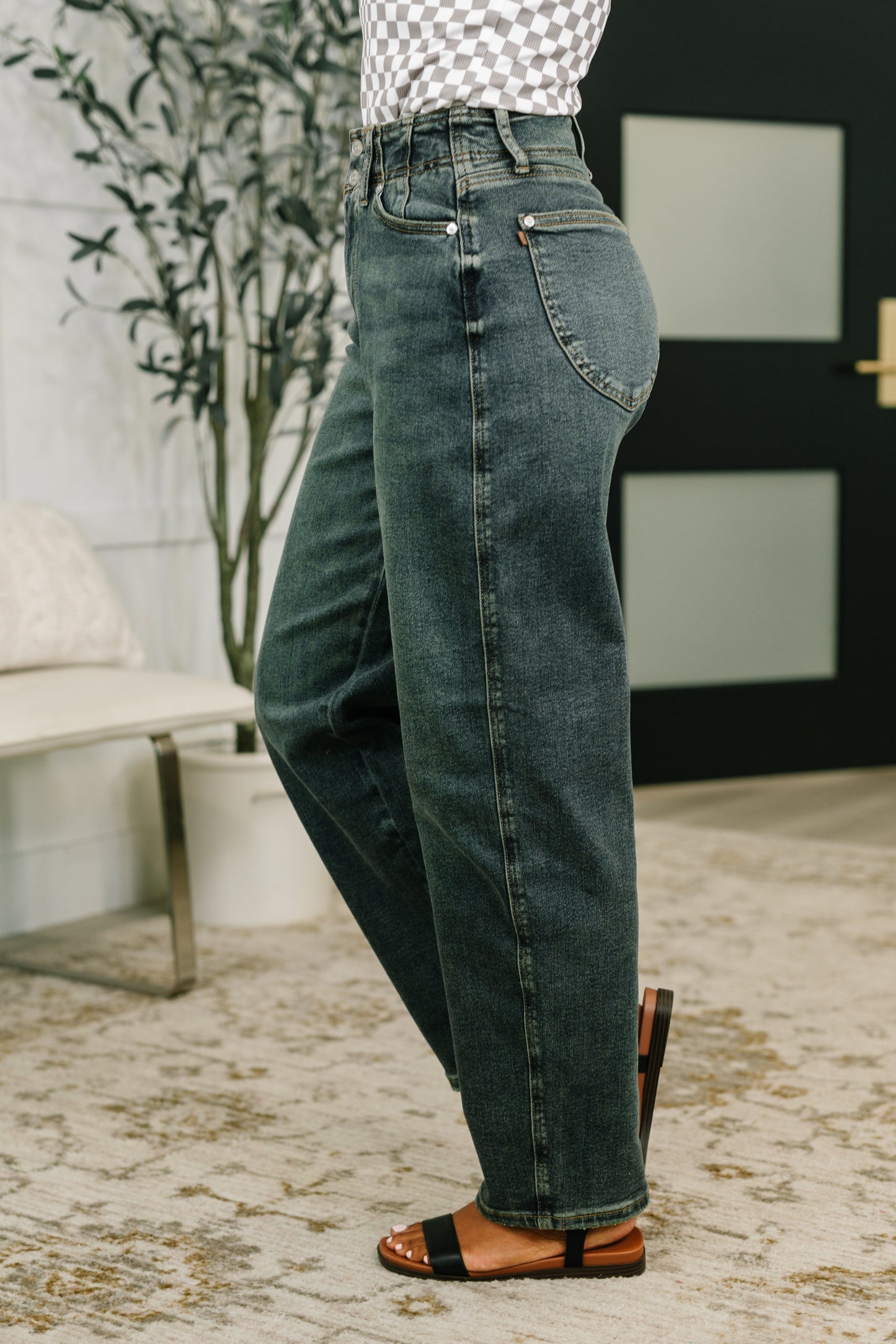 Person wearing high-waisted blue jeans standing outdoors with a plant and bench in the background.