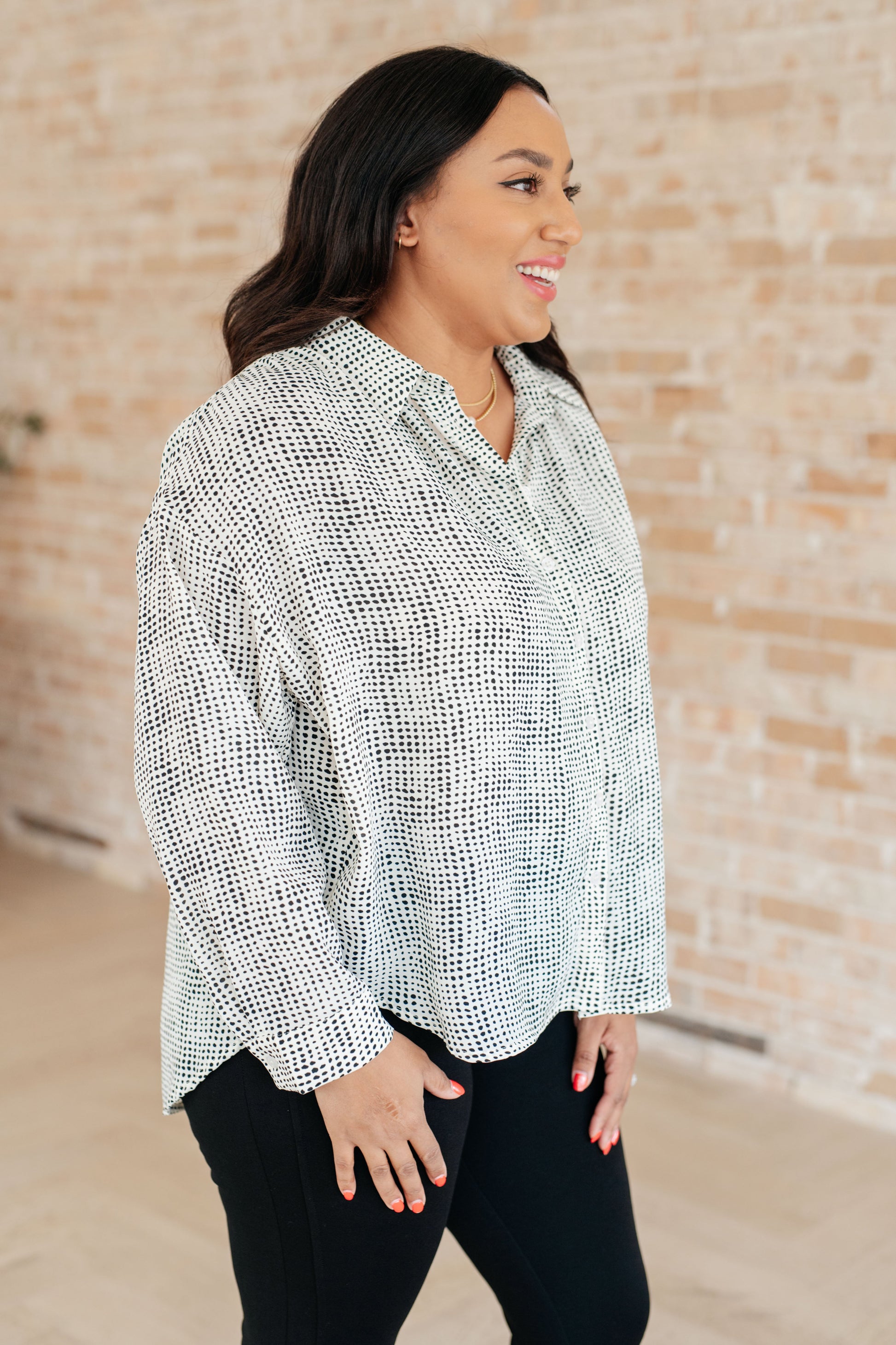 Woman wearing a patterned blouse against a brick wall.