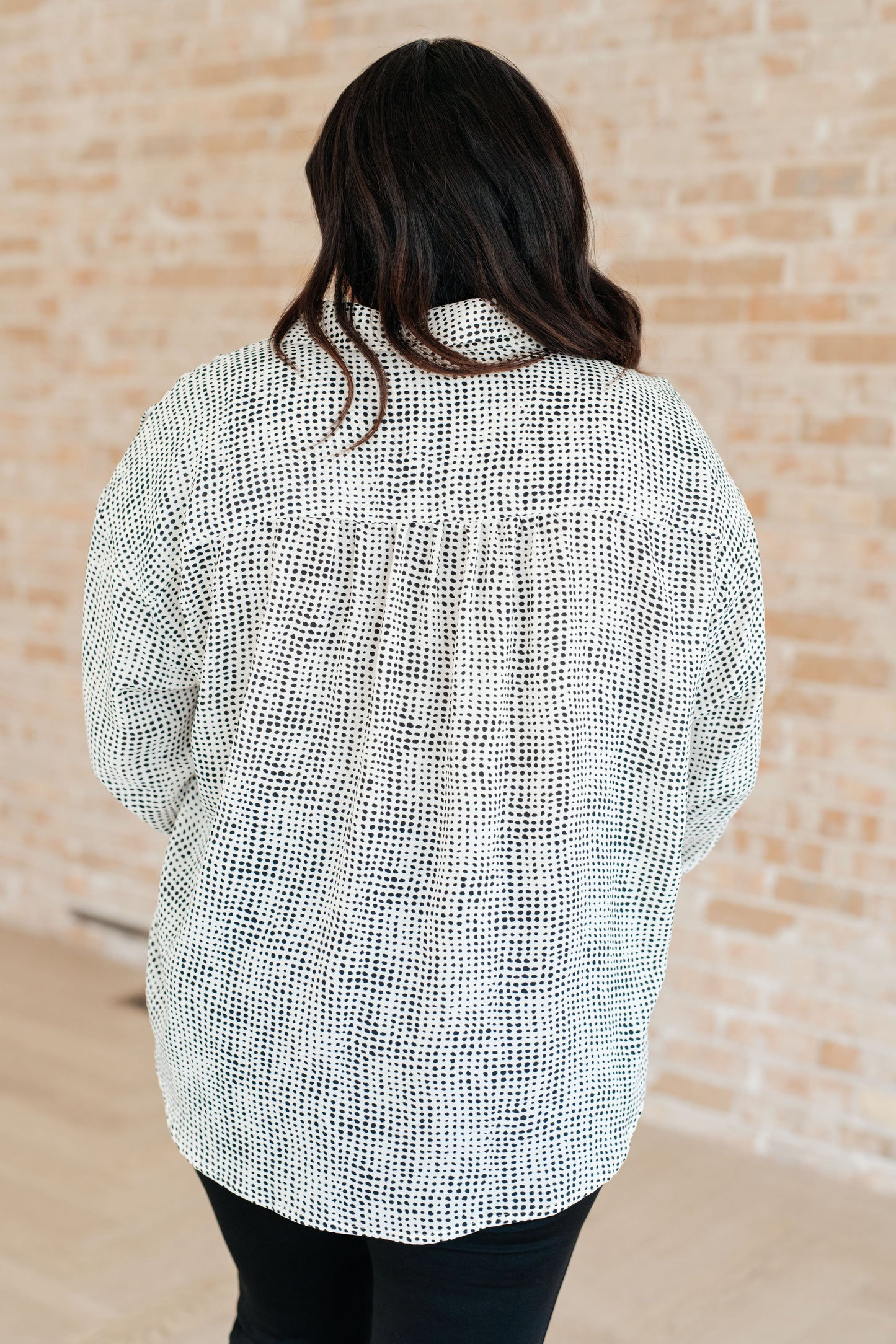 Person wearing a textured white and black shirt against a beige brick wall.