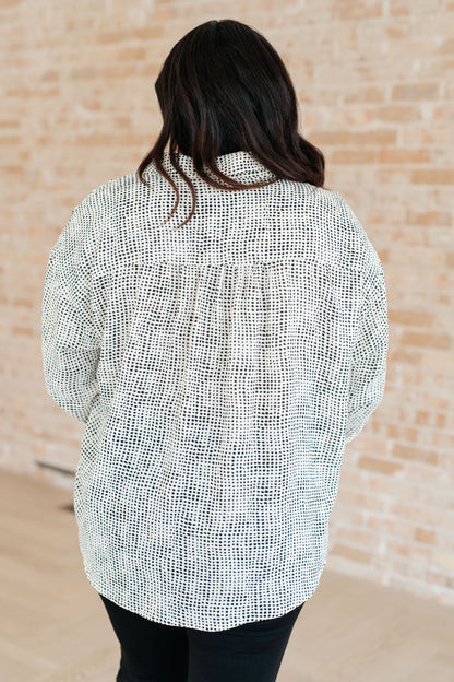 Person wearing a textured white and black shirt against a beige brick wall.