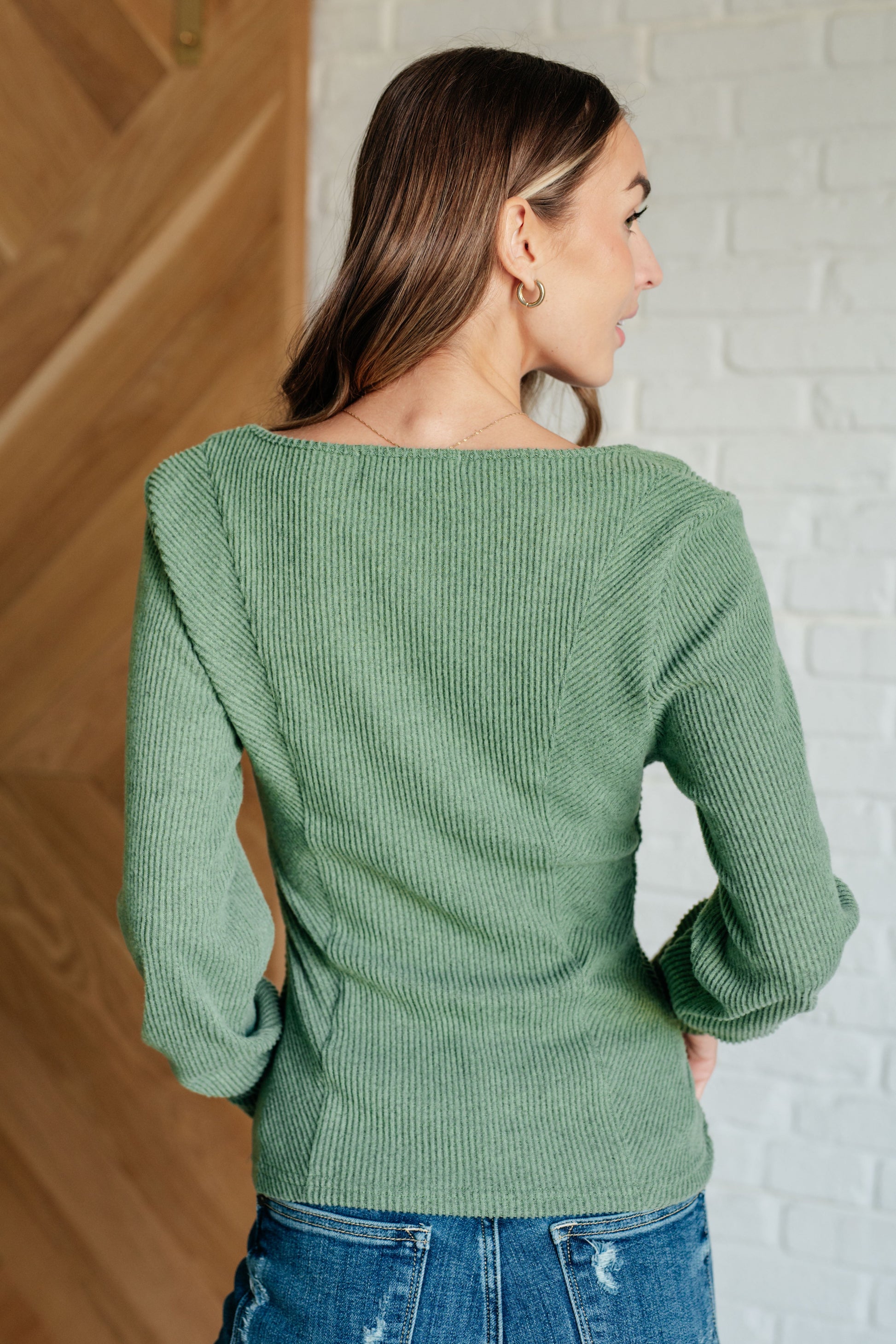 Woman wearing a green sweater with a white brick wall background