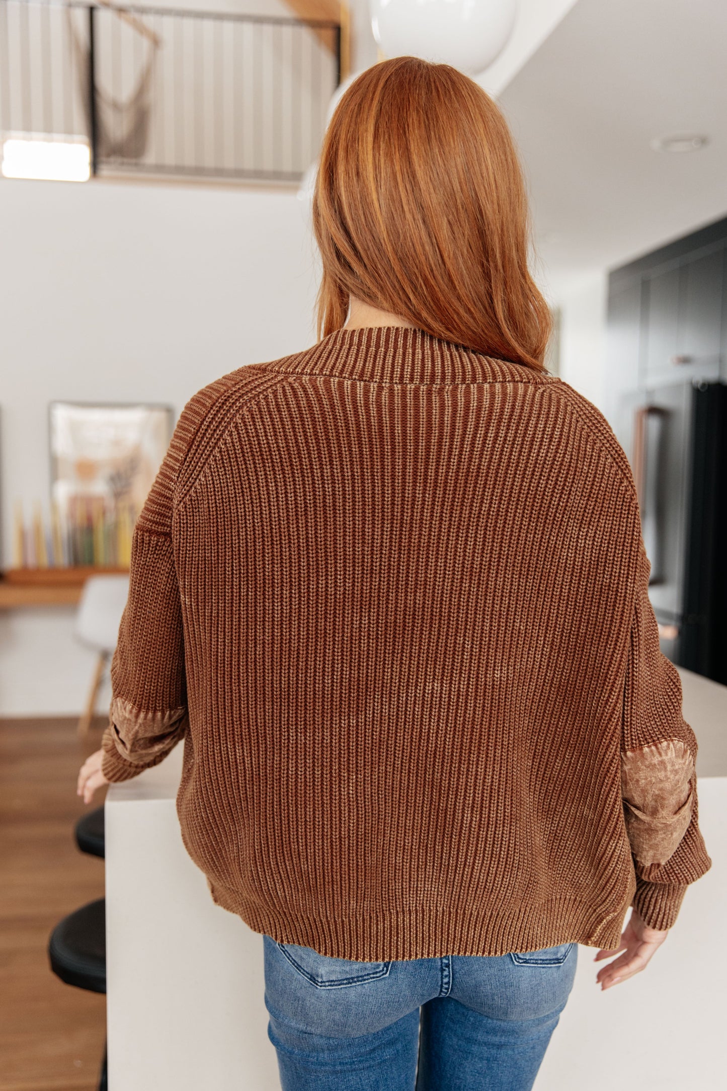 Person wearing a brown ribbed sweater in a modern kitchen.